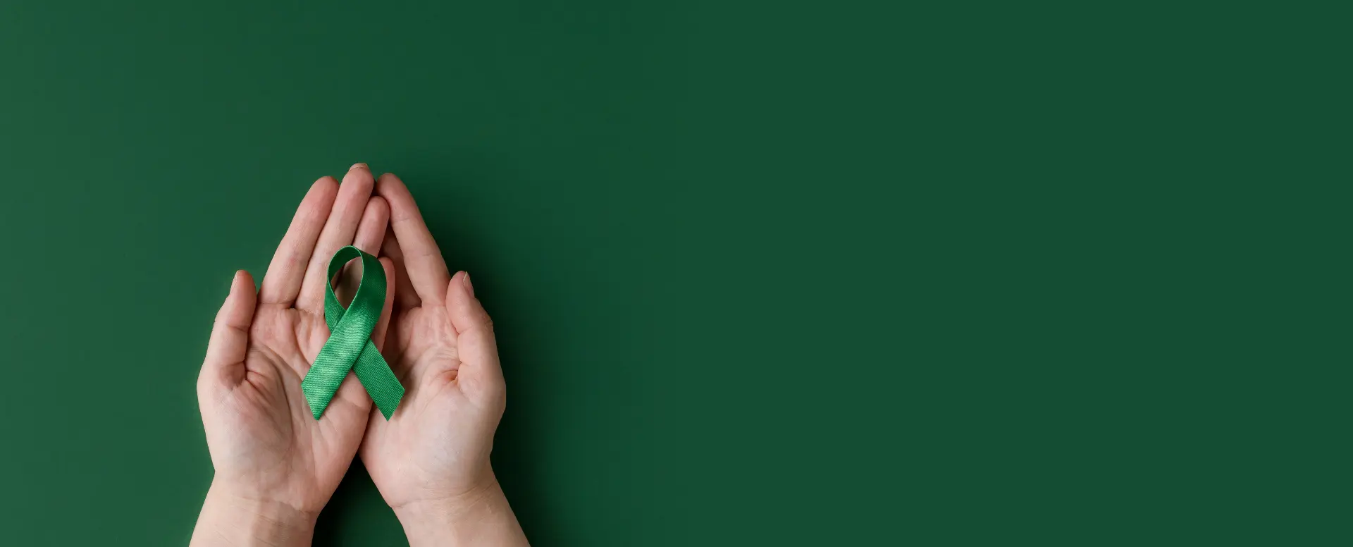 a pair of hands open facing upwards with a green mental health awareness ribbon in the palm